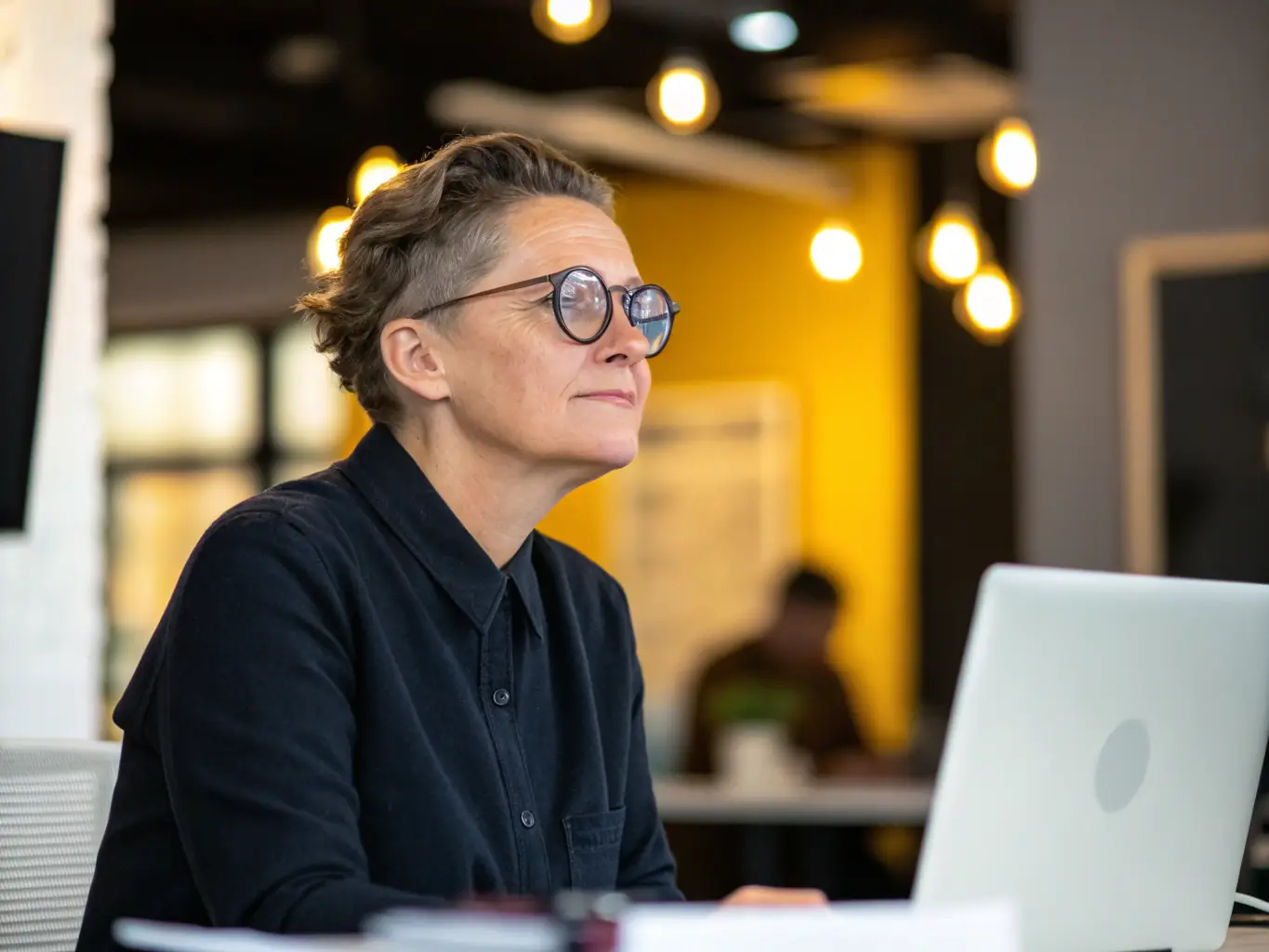 A person wearing classic, rectangular eyeglasses with a dark, tortoiseshell frame. The background is a well-lit office setting, suggesting professionalism and sophistication. The focus is on the frame's details and how it enhances the wearer's appearance.